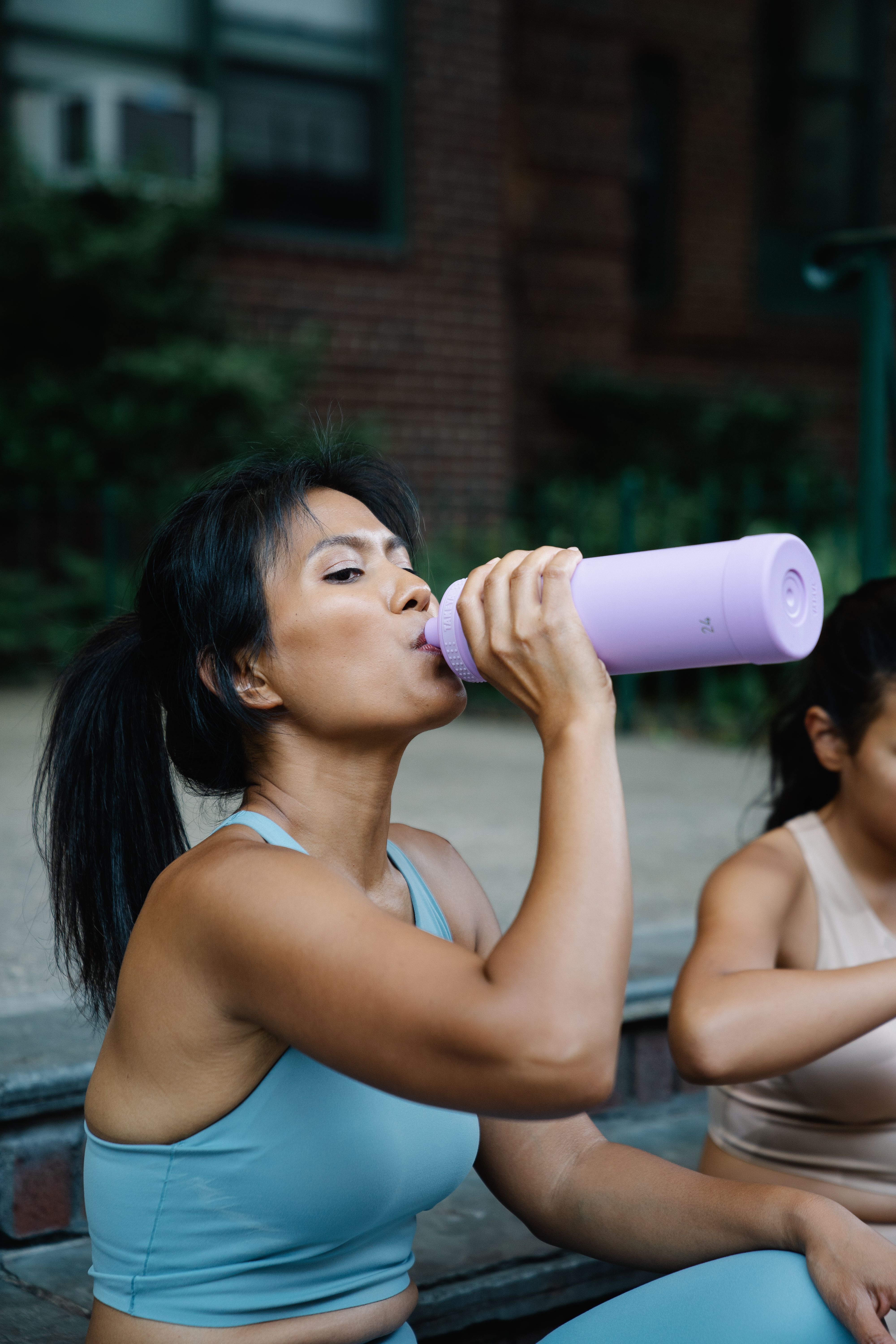 Woman drinking BCAA supplement powder next to a shaker bottle and gym equipment on a workout bench.