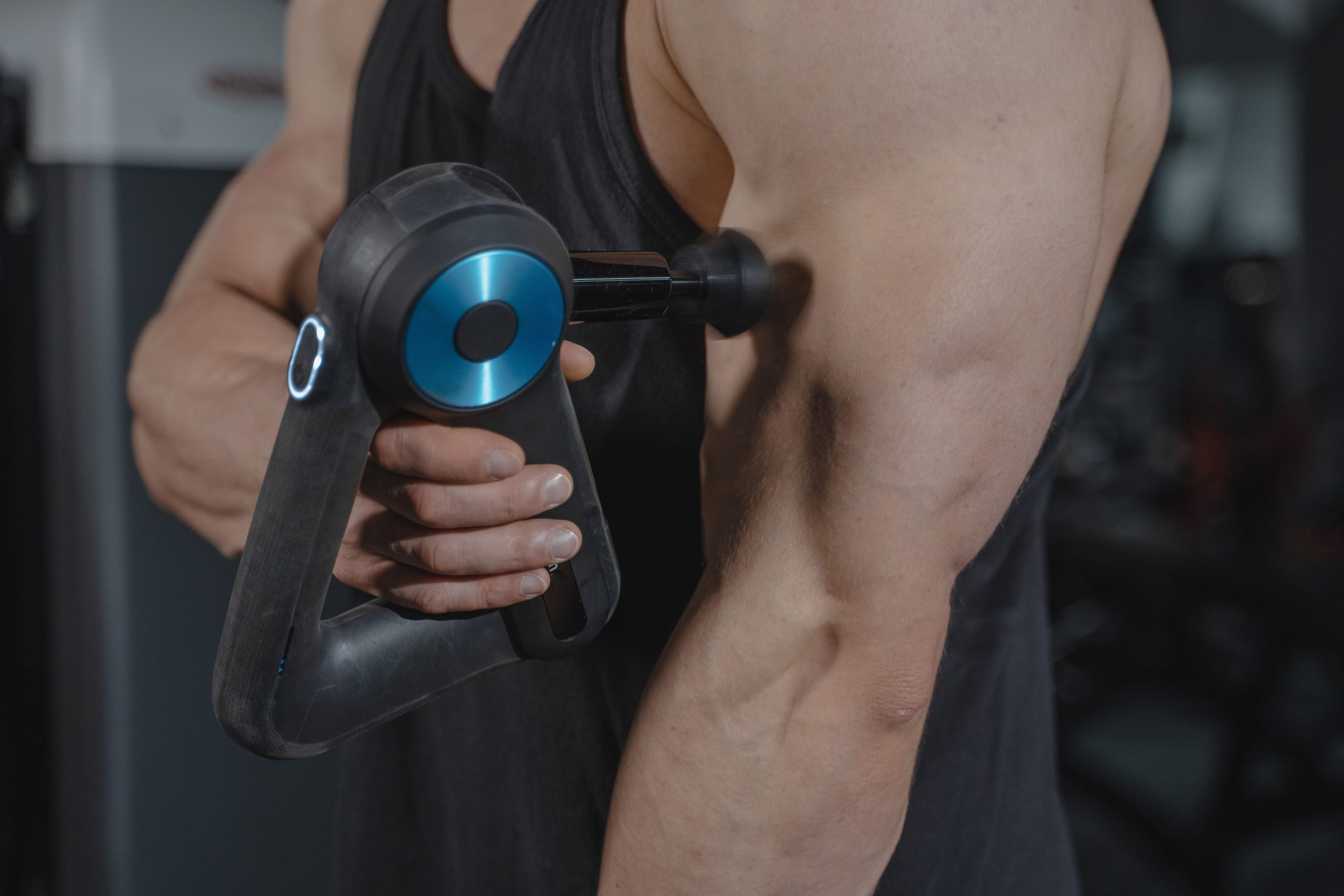 Person using a massage gun on their bicep muscles during a post-workout recovery session.