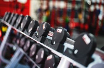 Assorted rubber-coated dumbbells arranged on a metal storage rack in a home gym setting.