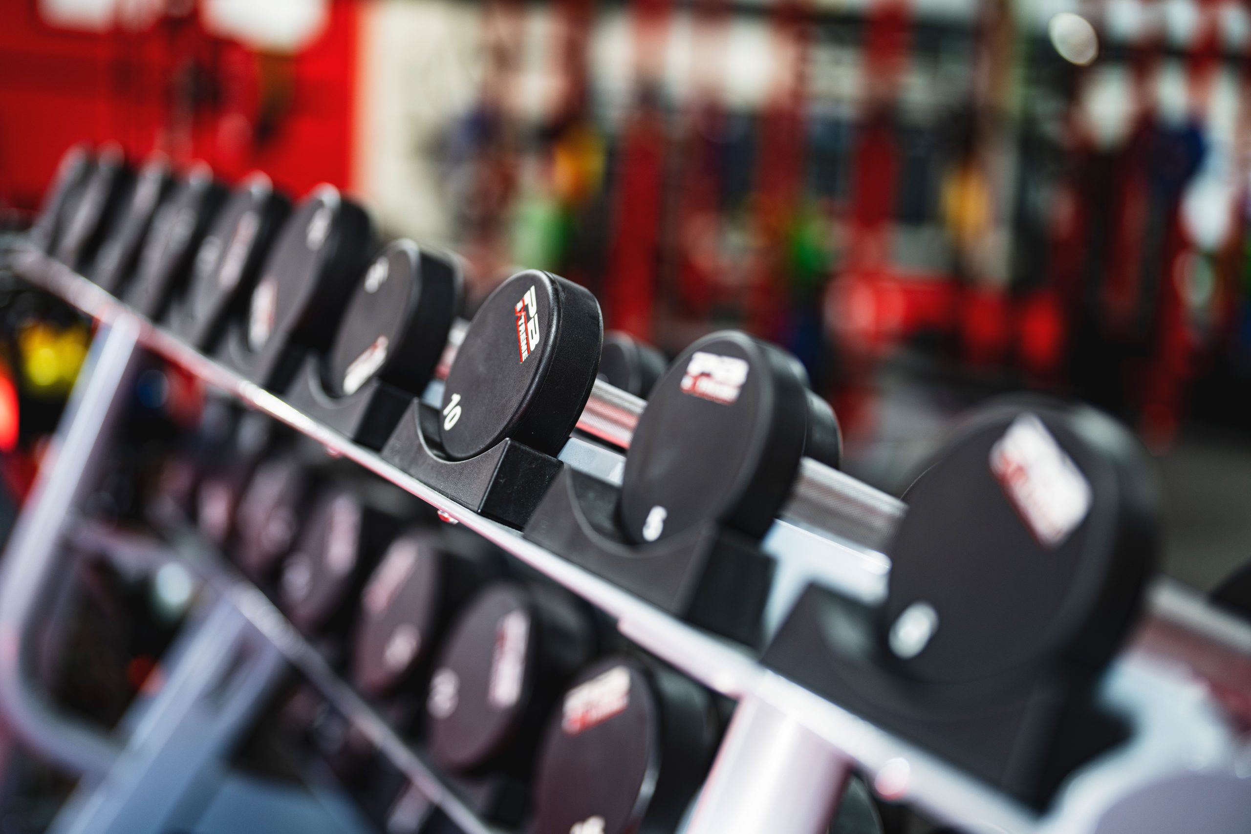 Assorted rubber-coated dumbbells arranged on a metal storage rack in a home gym setting.
