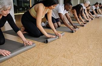 Woman unrolling a yoga mat on a wooden floor preparing for a home workout session.