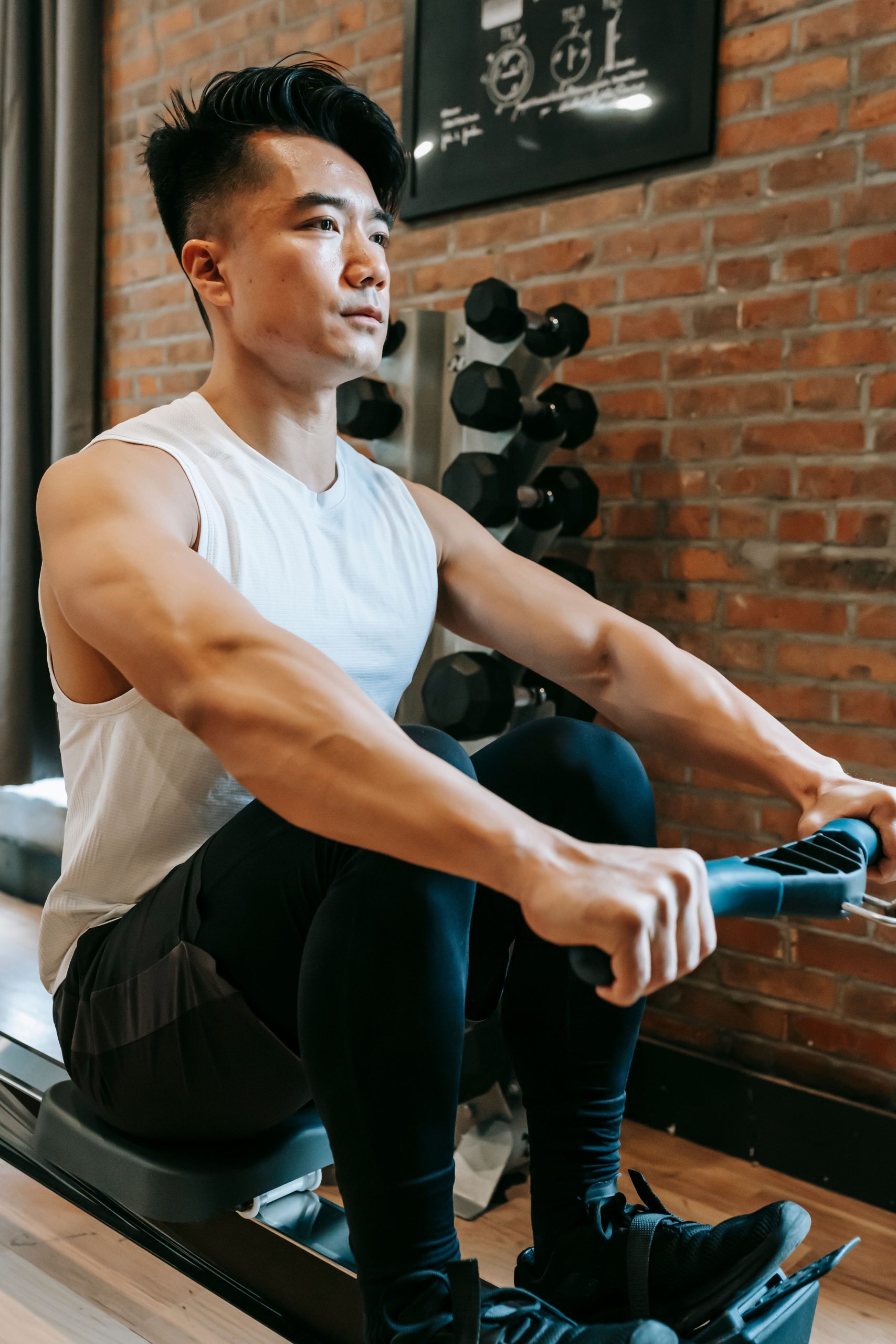 Person using a rowing machine in a bright home gym setting demonstrating proper rowing form.