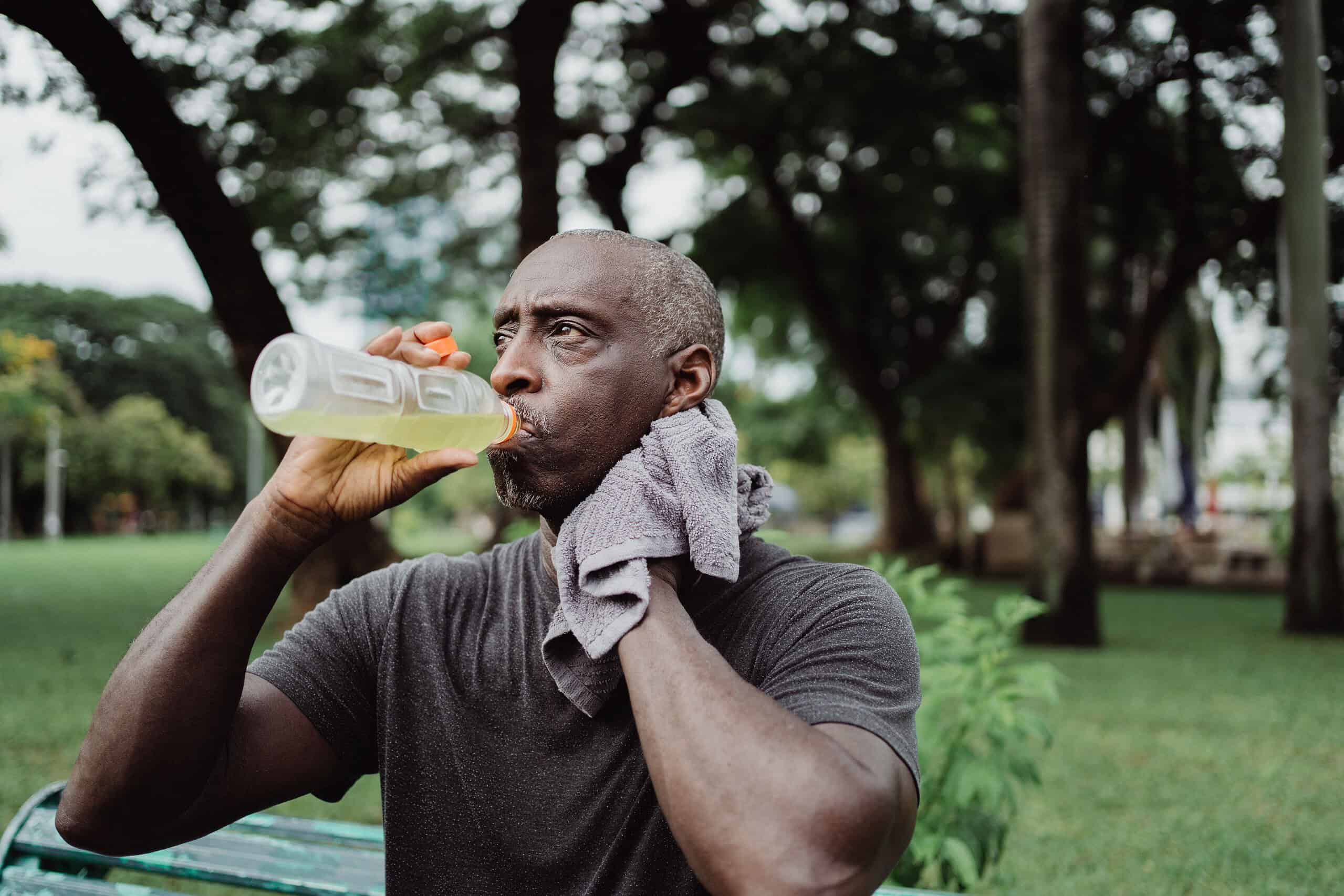 Man drinking an electrolyte drink from a bottle during an outdoor workout session.