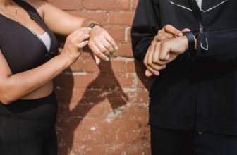 Side by side comparison of a smartwatch and slim fitness tracker on a workout surface.