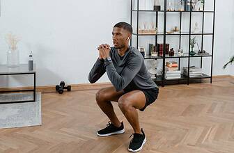 Man wearing athletic shorts performing a squat exercise in a modern home gym setting.