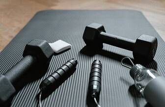 Collection of budget home workout equipment including dumbbells, jump rope, and foam roller on a gym mat.