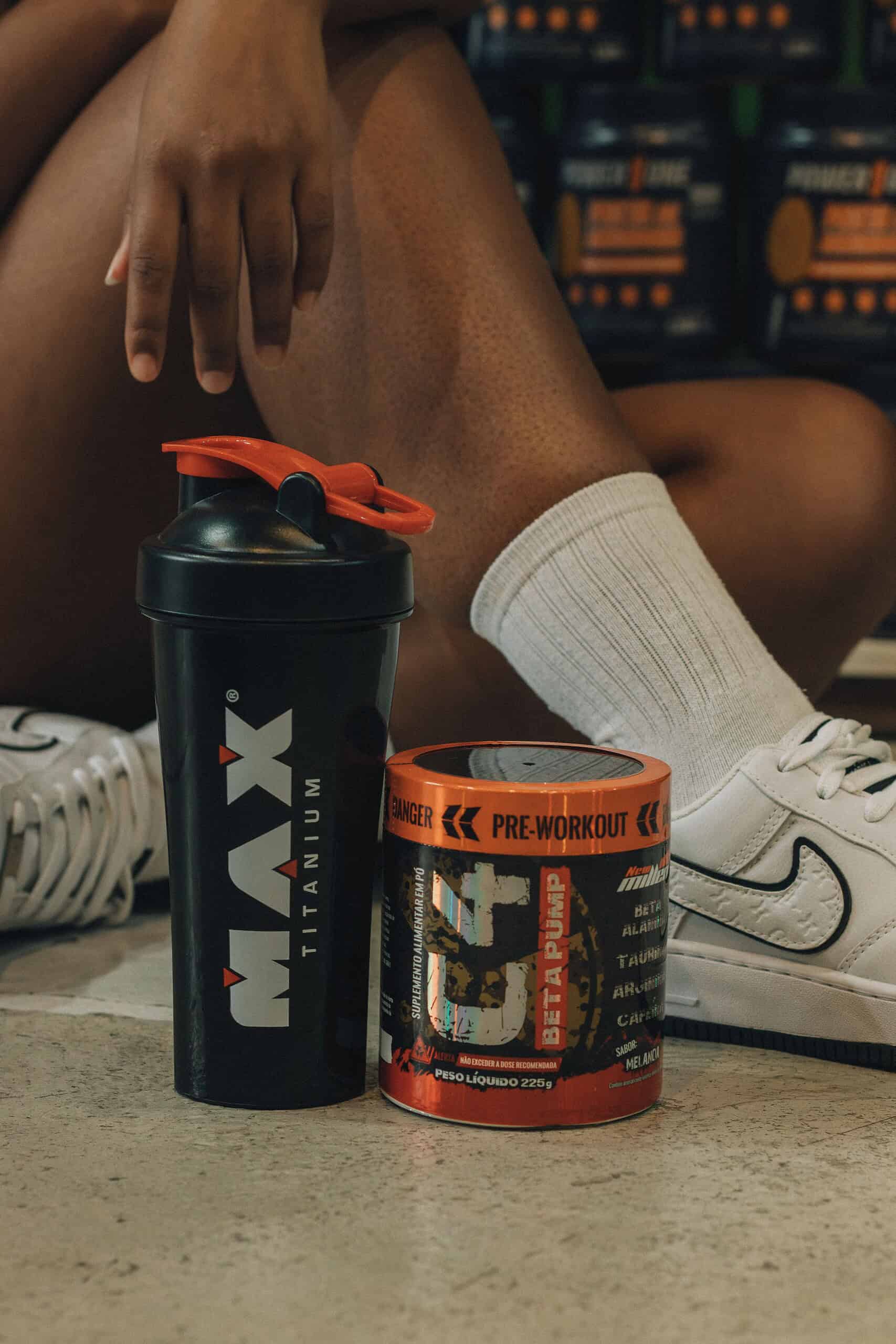 Pre-workout supplement powder in a scoop next to a shaker bottle and gym equipment on a workout bench.